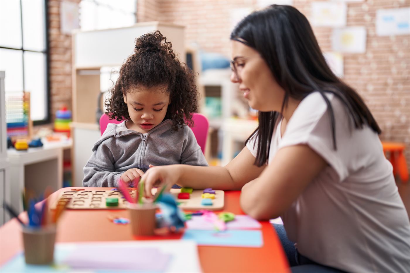 A teacher and toddler playing with a puzzle game at a table