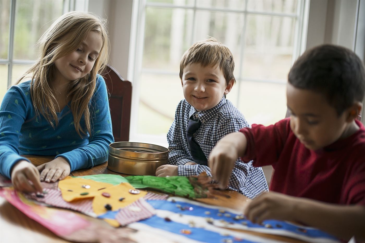 Three children making pictures with glue and stickers