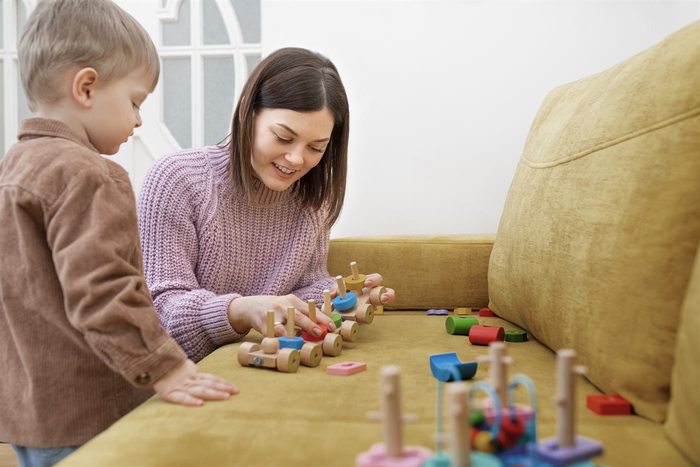 A caregiver and young boy playing together with colorful wooden toys