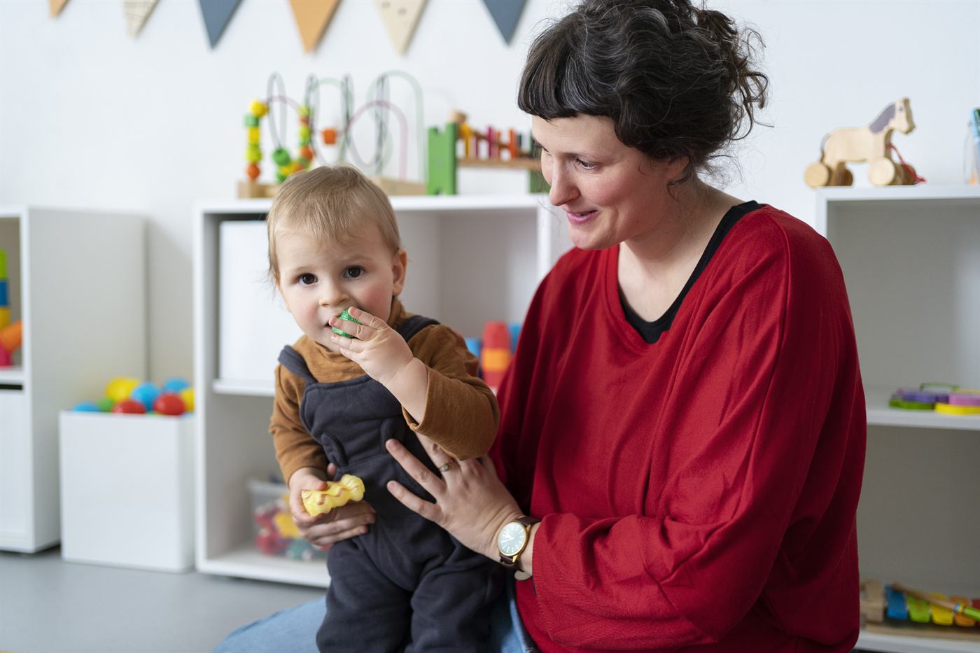 A therapist holding a smiling toddler in a playroom